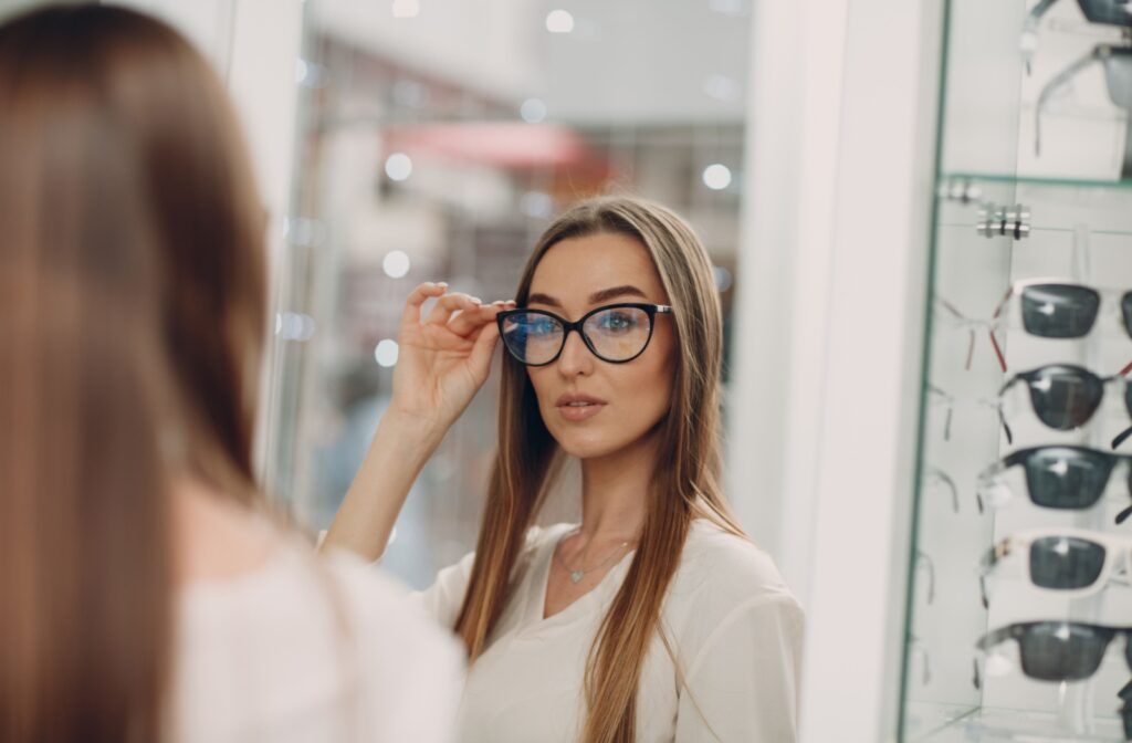 A woman looks in the mirror while she tries on a new set of cat-eyed glasses while searching for a trendy pair of glasses