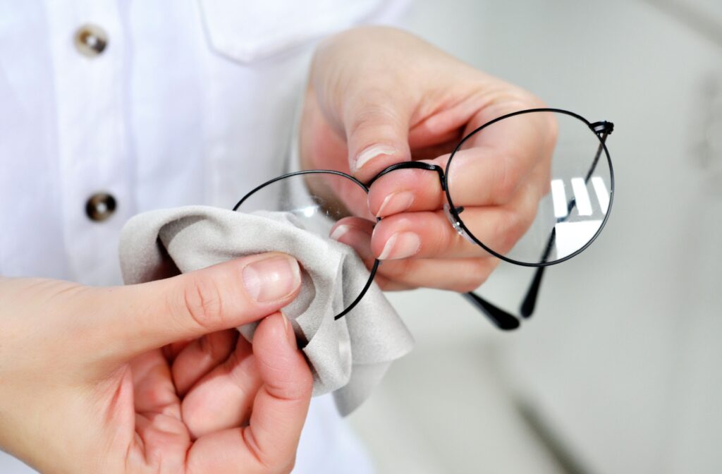 A person with clean, manicured hands cleans their eyeglasses with a microfiber cleaning cloth