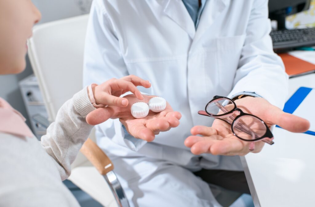 An optometrist holds out a pair of contact lenses and eyeglasses out for a young patient to choose from